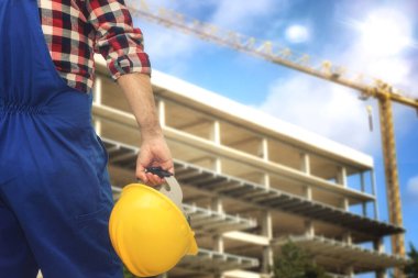 Kask ve koruyucu ekipman taşıyan işçiler inşaat alanındaki inşaat binalarına bakıyorlar.