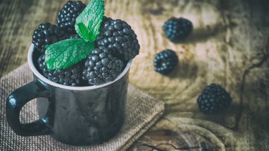 Taze böğürtlen ve ahşap masa üzerinde nane yaprakları.