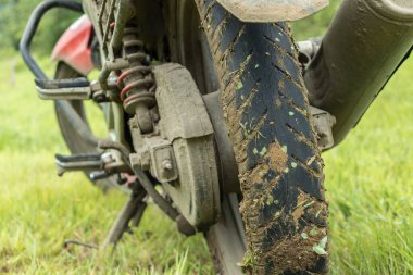 Arka planda yeşil çimenli uyarı lastiği olan çamurlu bir arazi bisikleti.