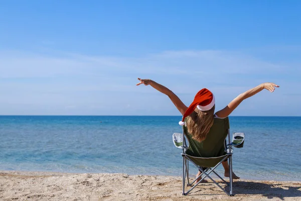 海のそばのビーチでの大晦日 クリスマスの帽子の女の子は太陽の下で日光浴をしています 青い空をコピースペースのように — ストック写真