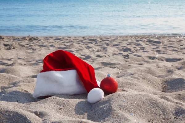 サンタは海のそばのビーチで赤い帽子 新年の休暇中の観光 砂の上のクリスマスの装飾 複写のためのスペース — ストック写真