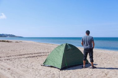 Denize yolculuk. Sahilde kamp yapmak. Deniz kenarında bir tatil. Kumda bir adam ve çadır