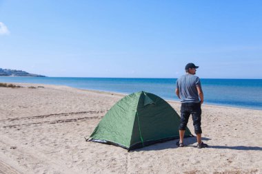 Denize yolculuk. Sahilde kamp yapmak. Deniz kenarında bir tatil. Kumda bir adam ve çadır