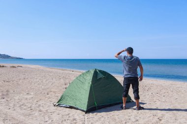 Denize yolculuk. Sahilde kamp yapmak. Deniz kenarında bir tatil. Kumda bir adam ve çadır