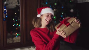 Kırmızı elbiseli kız yeni yıl hediyelerini açıyor. Noel gecesini kutlama konsepti. Tatil süsleri, Noel ağacı.