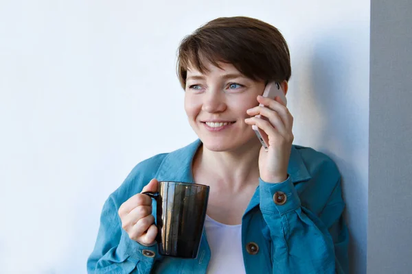 the concept of employment, interviews, advertising digital technology - woman drinking coffee and talking on the phone. Smiling woman with cup makes a call. Morning of girl