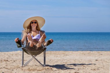Denize yolculuk. Mayolu ve şapkalı bir kız sahilde güneşleniyor. Kumsalda oturan bir turist. Boş zaman giysisi. Boşluğu kopyala