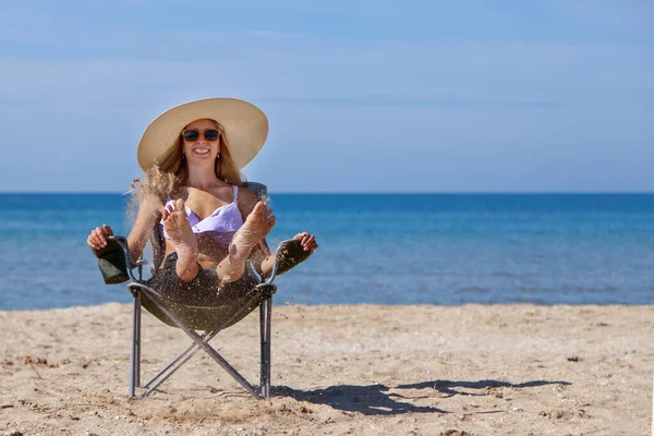 journey to the sea. girl in a bathing suit and hat sunbathing on the beach. tourist sitting on the sand. leisure wear. copy space