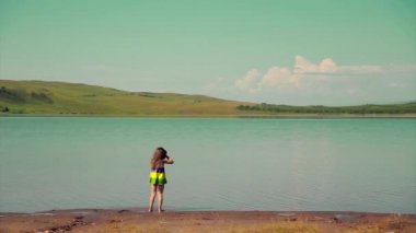 Kız nehrin kıyısındaki suda çiğniyor. Bir çocuk gölün kenarında oynuyor.