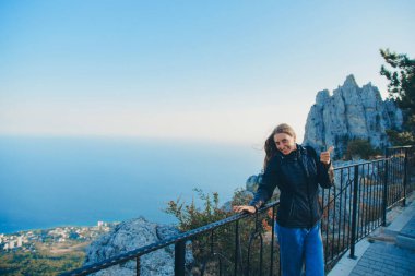 Sırt çantalı bir kız aydınlığın kenarında duruyor. Dağları aşın