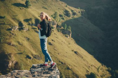 Sırt çantalı bir kız uçurumun kenarında duruyor. Dağları aşın
