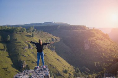 Sırt çantalı bir kız uçurumun kenarında duruyor. Dağları aşın