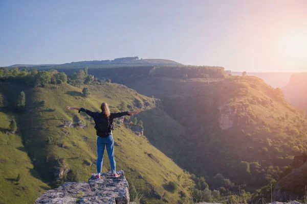Sırt çantalı bir kız uçurumun kenarında duruyor. Dağları aşın
