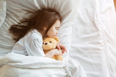 Bebek Taddy Bear 'la yatakta yatıyor. Küçük kız örgü bir oyuncakla uyuyor.