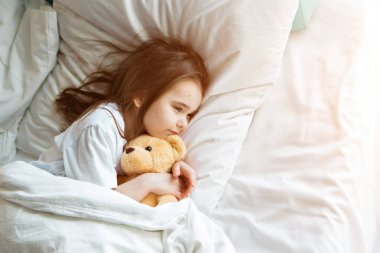Bebek Taddy Bear 'la yatakta yatıyor. Küçük kız örgü bir oyuncakla uyuyor.