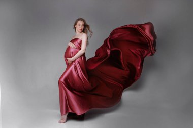 Kırmızı elbiseli hamile kız. Açık arkaplanda güzel kumaş dokusu