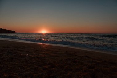 dalgalar denizin kayalık kıyılarını yıkar. Günbatımı. Köprünün suyundaki yansıma ve ışınlar