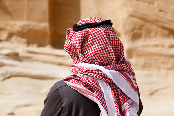 Al Ula, Saudi Arabia, February 19 2020: A Saudi Arabian tourist with traditional headdress stands in front of a grave in Al Ula