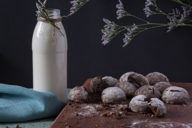 Süt şişesi, ağaç dalları ve siyah arka planda ev yapımı çikolatalı kurabiyeler..