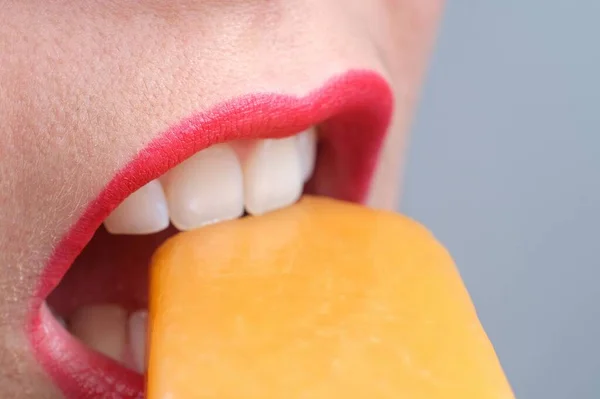 Close up of a young woman\'s mouth with red lips and beautiful white teeth, biting an ice cream