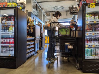 Kirkland, WA / USA - Nisan 2020: Koronavirüs salgınının ortasında QFC 'deki bir kasada pleksiglas bariyeri arkasında kontrol ederken koruyucu maske ve eldiven takan kadın.