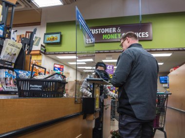 Kirkland, WA / USA - Nisan 2020 civarı: Koronavirüs salgını sırasında Fred Meyer 'in bakkal dükkanının kasasında bir pleksiglass duvarın arkasında kasiyer