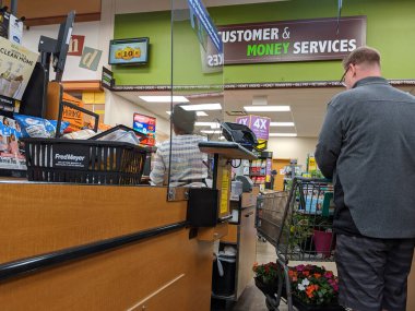 Kirkland, WA / USA - Nisan 2020 civarı: Koronavirüs salgını sırasında Fred Meyer 'in bakkal dükkanının kasasında bir pleksiglass duvarın arkasında kasiyer