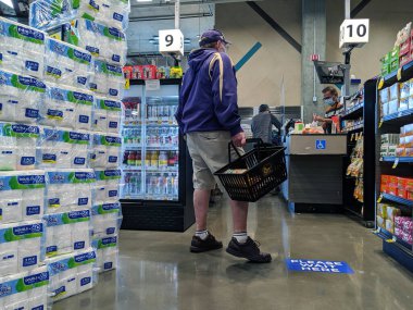 Kirkland, WA / USA - Nisan 2020 dolaylarında: QFC marketinde beklerken maske takan yaşlı bir adam, sosyal uzaklık işaretlerine dikkat ediyor
