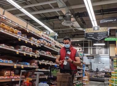 Kirkland, WA / USA - Nisan 2020 civarı: Ekmek stoklarını tarayan ve rafları dolduran market çalışanı, COVID-19 salgını sırasında yüz maskesi takıyordu.