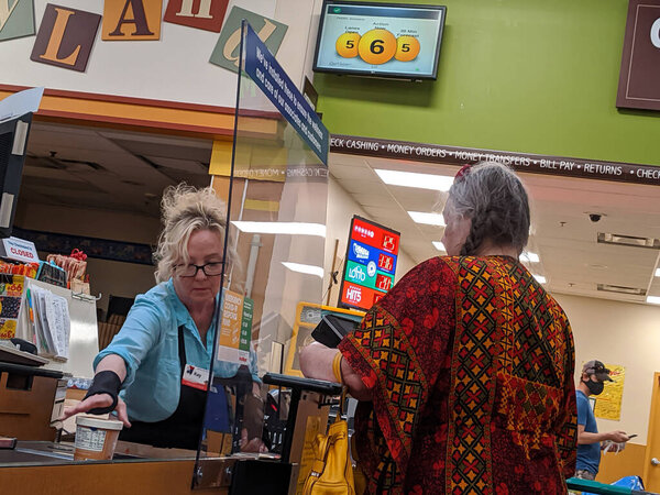 Kirkland, WA / USA - circa April 2020: Cashier behind a plexiglass wall at a checkout counter inside a Fred Meyer grocery store during the coronavirus outbreak