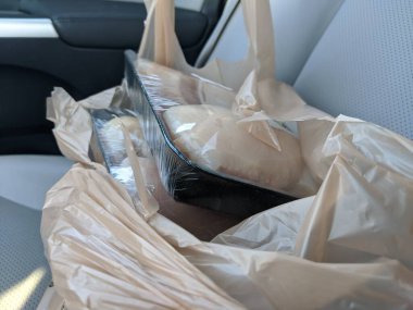 Market gezisinden sonra arabada duran kahverengi bir poşetin içinde çözülmüş tavuk göğsü paketleri var.