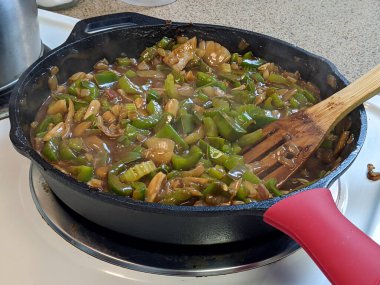 Kırmızı ve sarı soğan, sarımsak, dolma biber ve kereviz dolu dökme demir tavanın yan açısı.