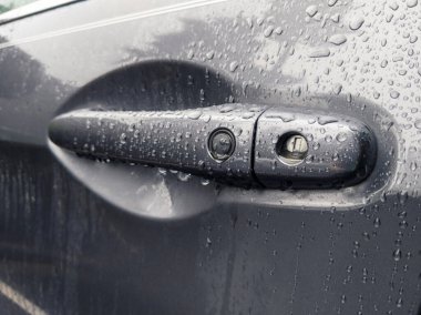 Kuzeybatı Pasifik 'teki fırtınadan sonra yağmur damlalarıyla kaplı gri bir araba kapı kolunun açılı görüntüsü.
