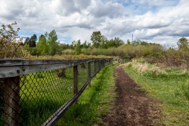 Güneşli bir günde, bulutlarla dolu bir çiftlikte çitlerle çevrili toprak bir yolun güzel manzarası.