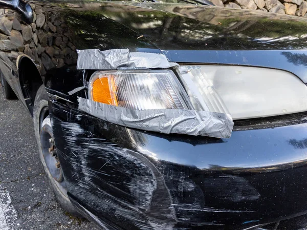Zbliżenie Poważnego Uszkodzenia Przedniego Zderzaka Reflektora Czarnego Samochodu Połączone Taśmą — Zdjęcie stockowe
