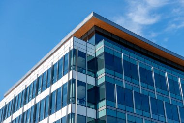 Geniş açılı, pencereyle kaplı bir binanın köşesi mavi, bulutlarla dolu bir gökyüzüne karşı.