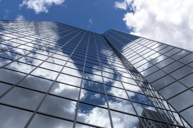 Geniş açılı, pencereyle kaplı bir binanın köşesi mavi, bulutlarla dolu bir gökyüzüne karşı.