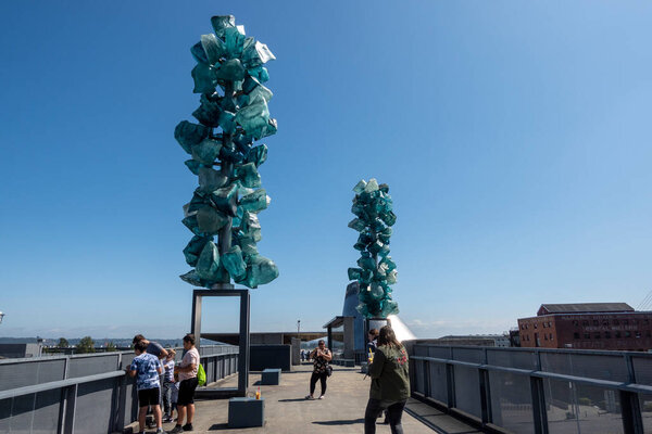 Tacoma, WA USA - circa August 2021: View of large sculptures and tourists outside of the Museum of Glass downtown on a sunny, cloudless day.