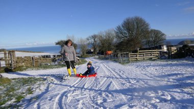 Kadın ve çocuk karda kızakla eğleniyor.