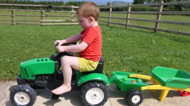 Kızıl saçlı çocuk bahçede oyuncaklarla oynuyor.