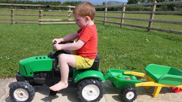 Kızıl saçlı çocuk bahçede oyuncaklarla oynuyor.