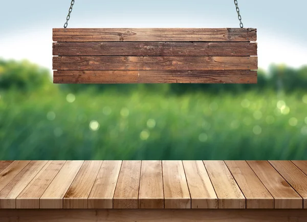 Mesa de madera con letrero de madera colgante sobre fondo borroso naturaleza verde — Foto de Stock