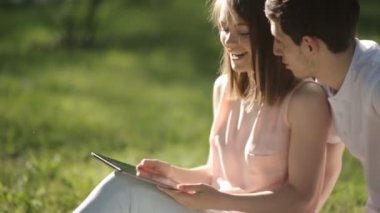 Kız parkta oturan ve tablet vasıl bakarak herifle. Yakın çekim.