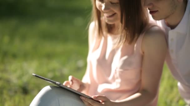 Killen med flickan sitter i parken och titta på Tablet PC. Närbild. — Stockvideo