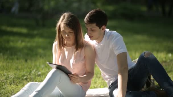 El tipo con la chica sentada en el parque y mirando la tableta — Vídeos de Stock