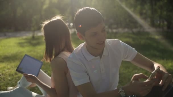 Pojke och flicka sitter rygg mot rygg på Pläd i parken. närbild. — Stockvideo