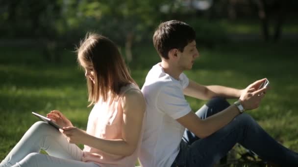 Ragazzo e ragazza seduti schiena contro schiena sul plaid nel parco — Video Stock