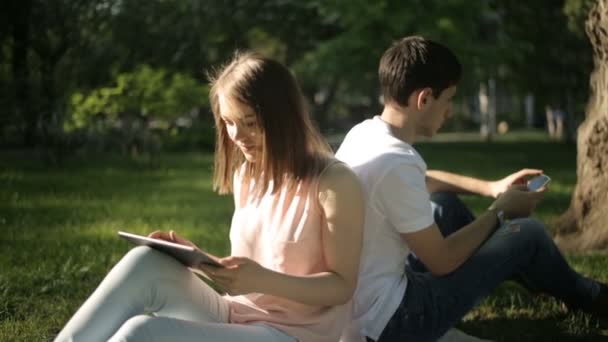 Chłopak i dziewczyna siedzi z powrotem do tyłu na kratę w parku — Wideo stockowe