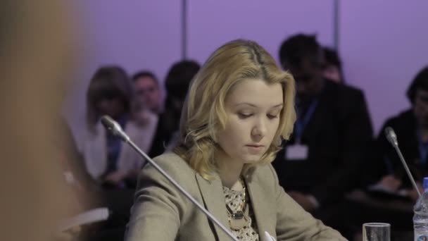 Une femme adulte écoute le rapport de l'orateur lors d'un forum économique et écrit tout dans son carnet. Salle de réunion à la table ronde. Conférence de presse . — Video