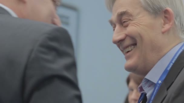 Hombre de negocios adulto feliz con el pelo gris se está comunicando con alguien en el Foro Económico Internacional. Dos hombres bromean entre sí para un buen evento . — Vídeo de stock